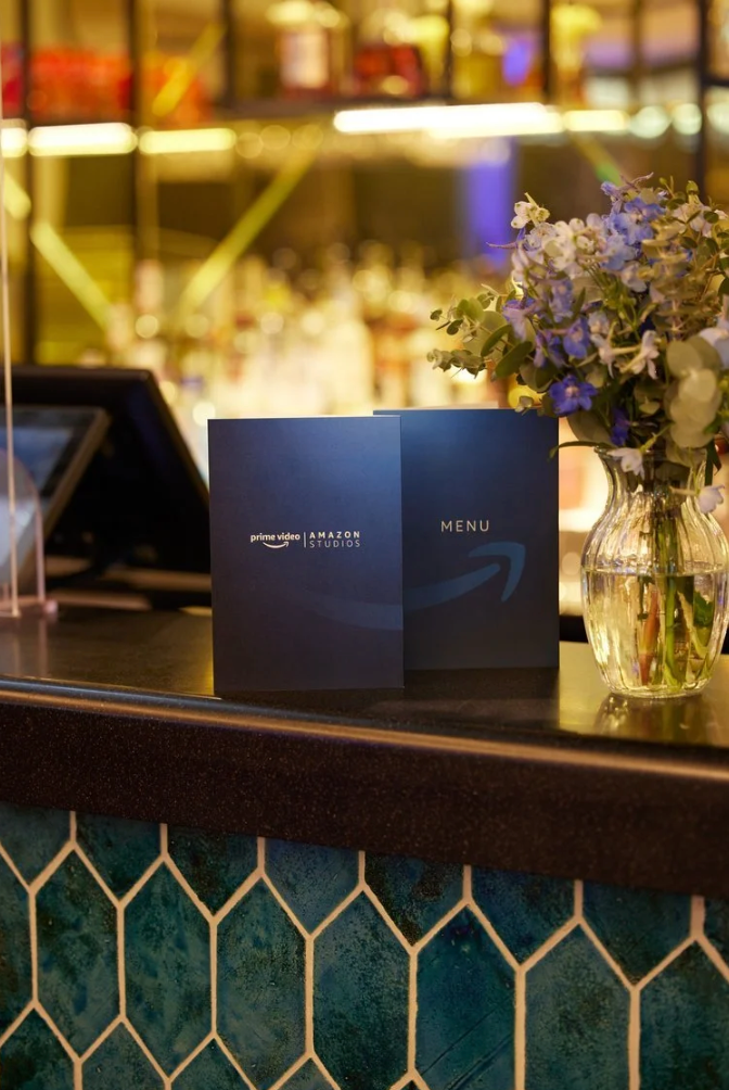 A menu and floral arrangement sit on a bar counter with decorative teal and gold geometric tile detail.