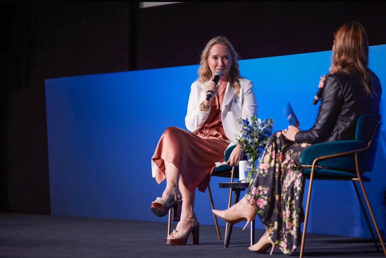 People seated in chairs against a bright blue backdrop during what appears to be an interview or panel discussion.