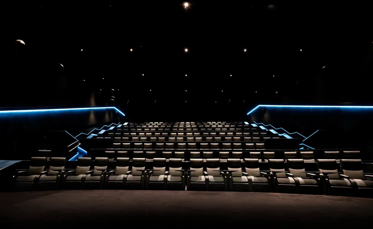 Empty theater auditorium with blue accent lighting highlighting rows of seats in darkness.