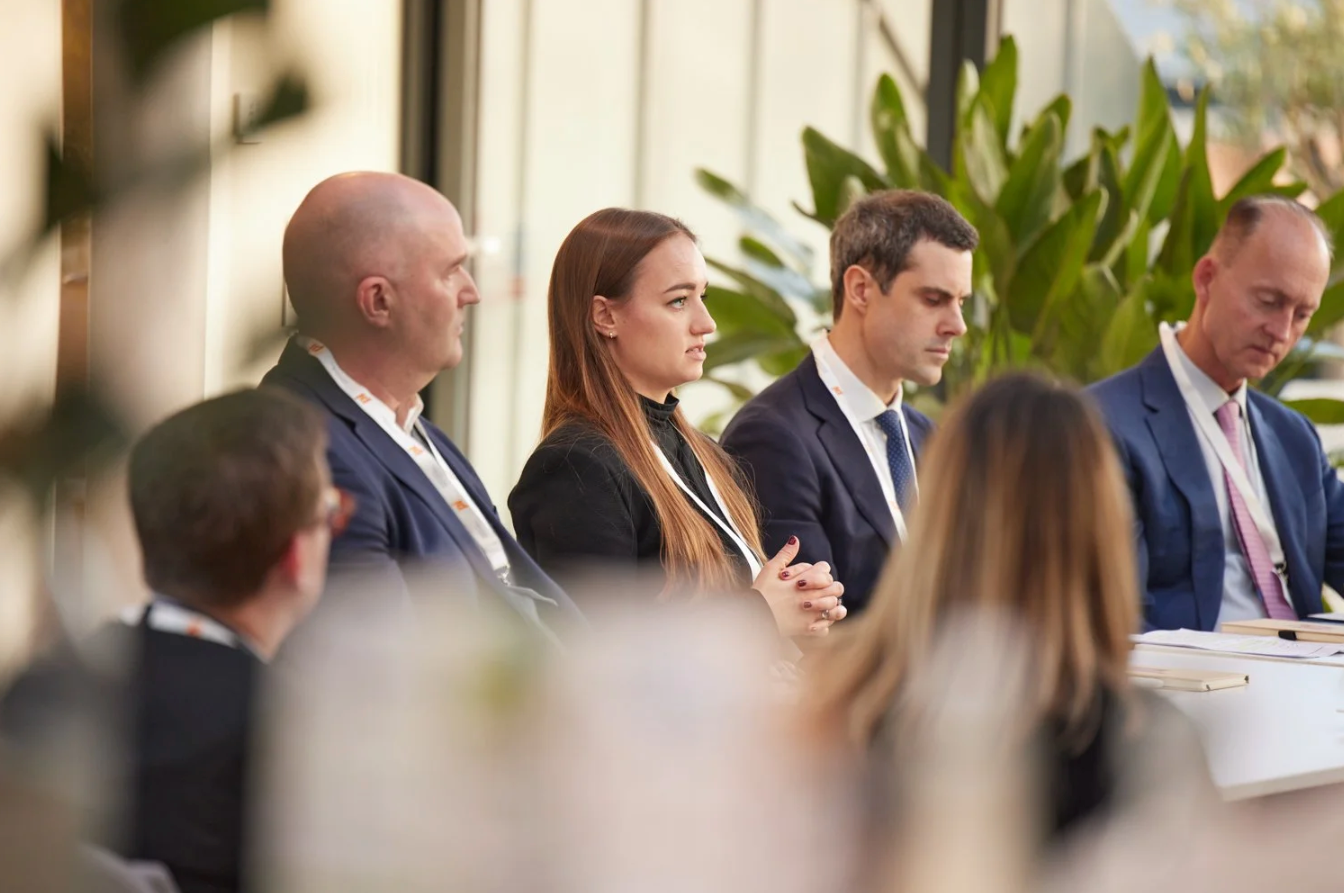 Business professionals seated at a conference table during a corporate meeting with natural lighting.