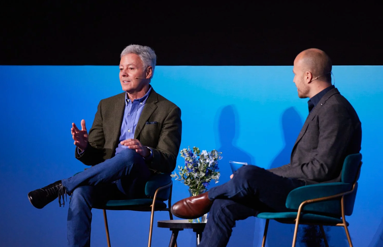 Panel discussion participants seated in chairs against a blue backdrop at a professional event.