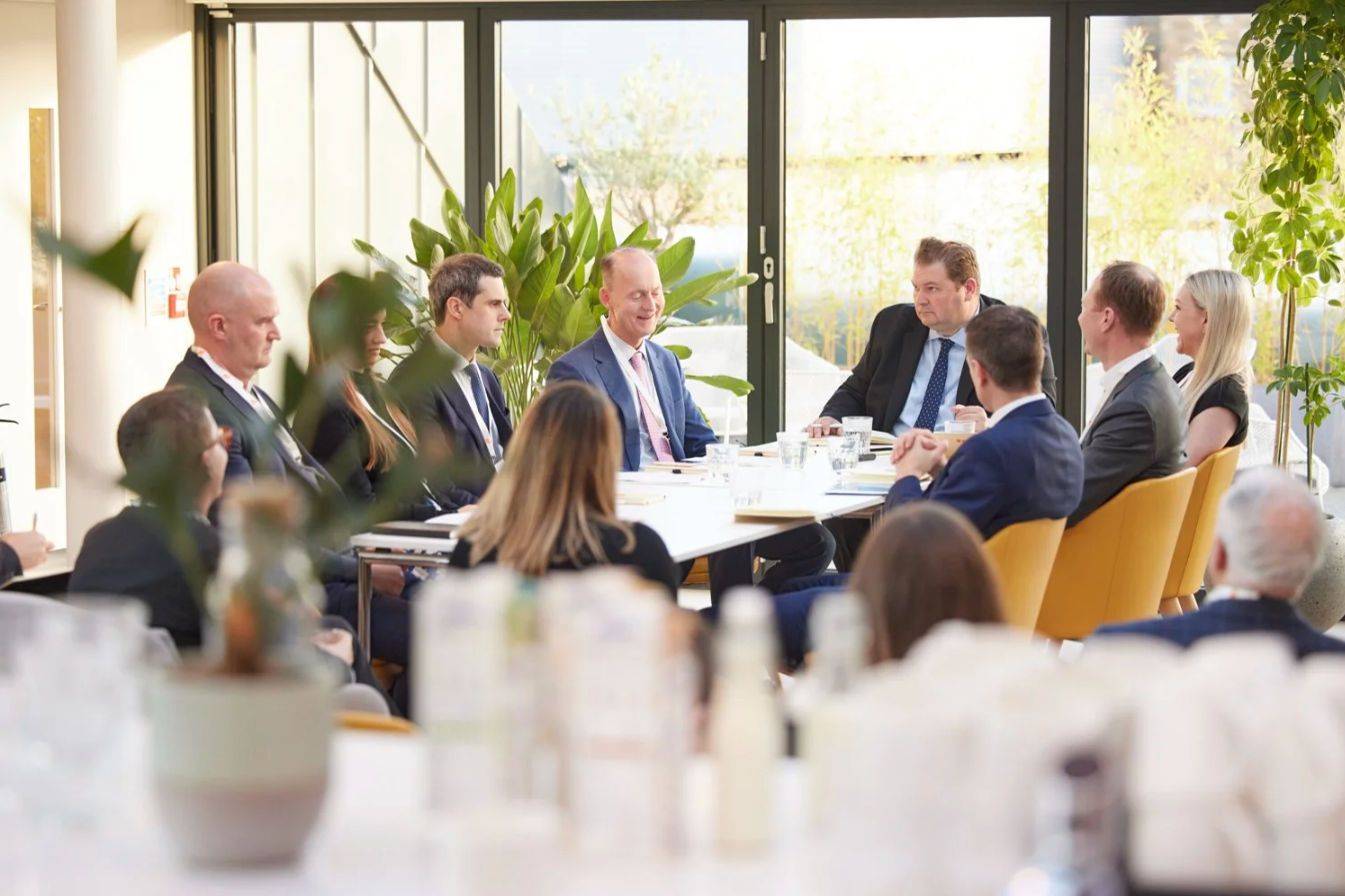 Business professionals gather around tables in a bright modern office space during a corporate meeting or event.