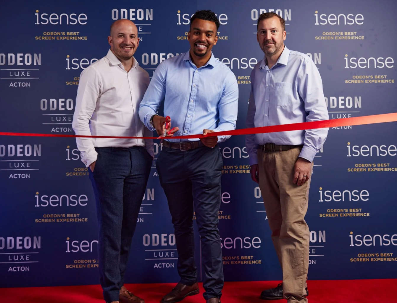 Three people in business attire stand at a ribbon cutting ceremony with Odeon and Isense branded backdrop.