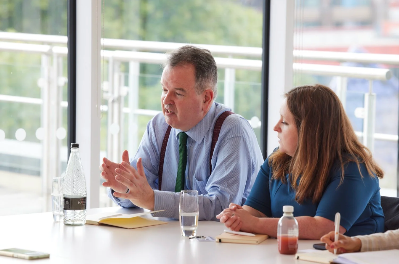 Two business professionals in a bright meeting room having a discussion at a conference table with water glasses.