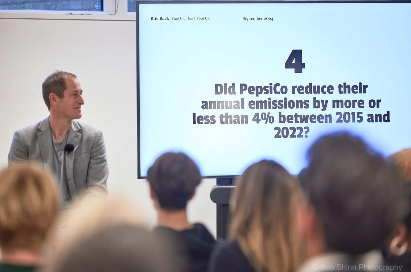 Business conference presentation showing text and graphs about PepsiCo emissions on large display screens.