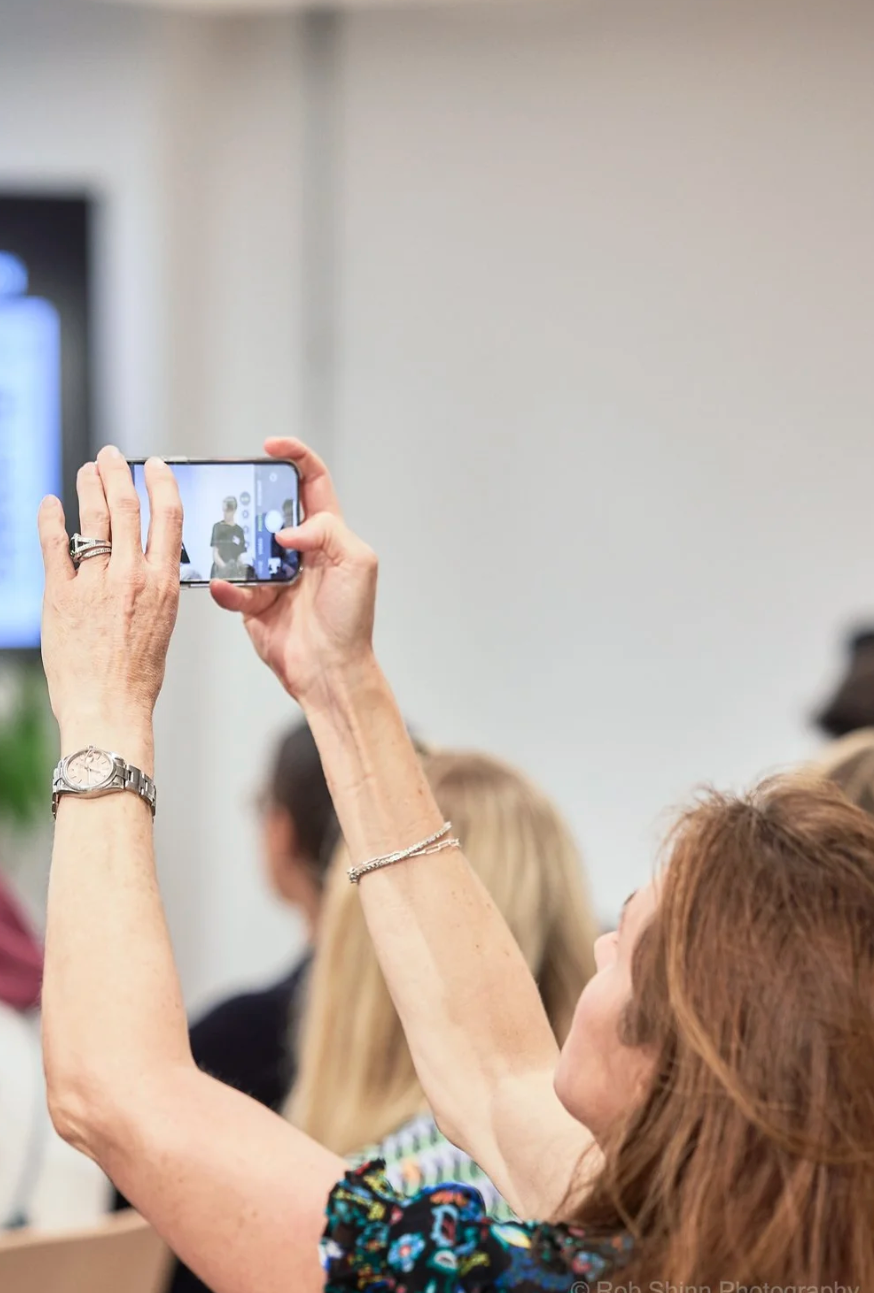 A row of hands holding up smartphones to take photos at an event.
