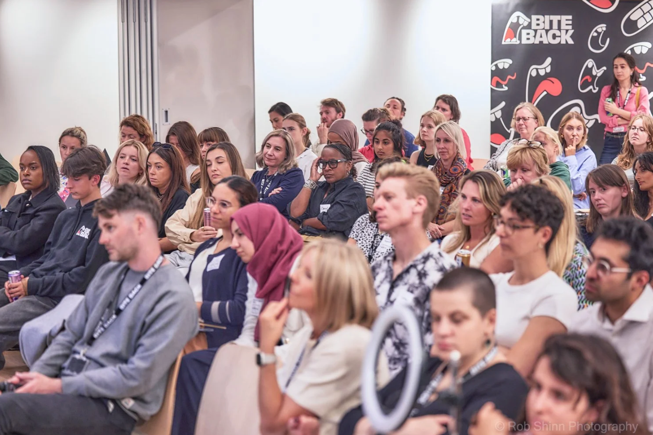 Audience members seated in rows at a conference or presentation event showing engaged expressions and attentive postures.