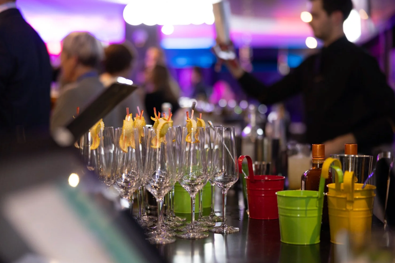 Empty cocktail glasses lined up at a bar under purple and blue ambient lighting create a festive nightclub atmosphere.