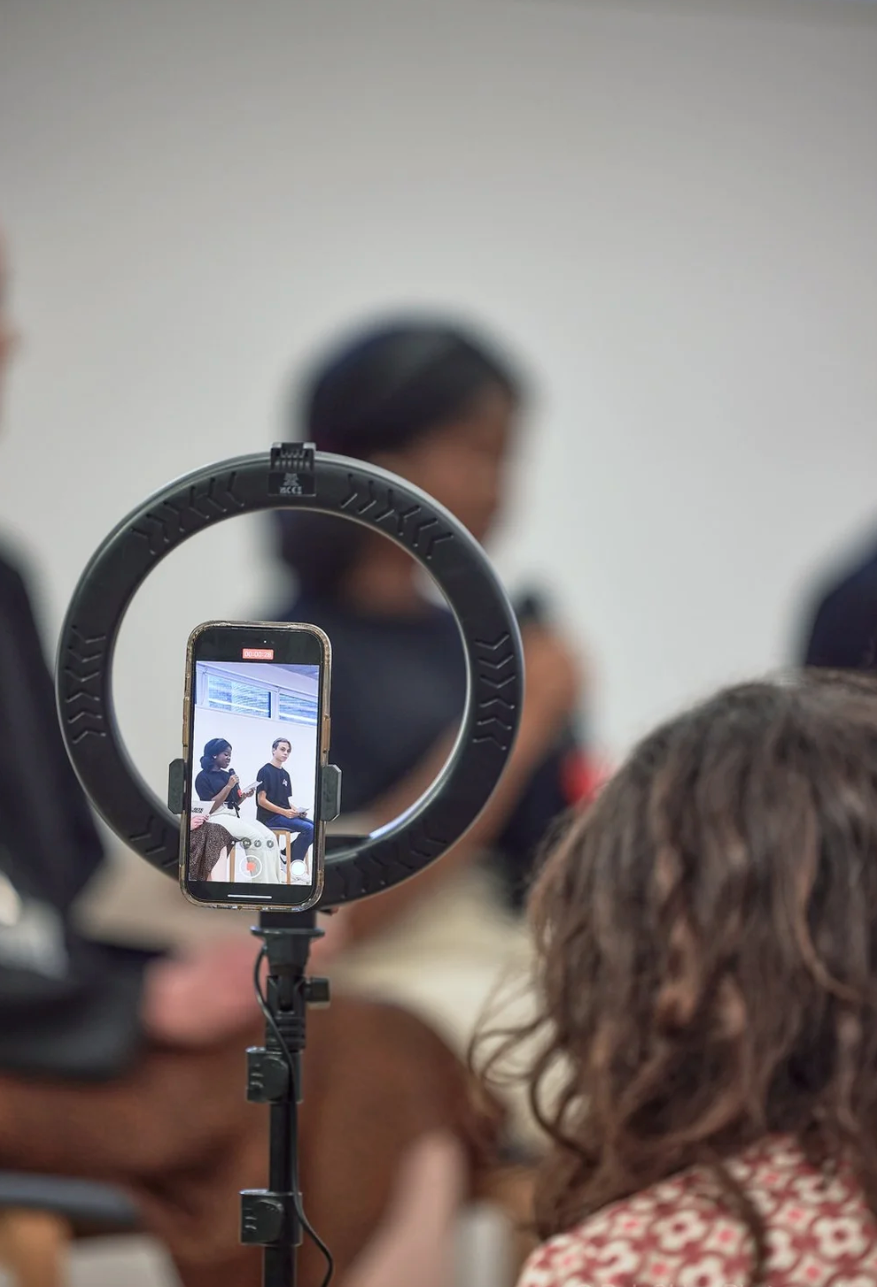 A ring light illuminates a phone screen during a video call or virtual meeting in a classroom setting.