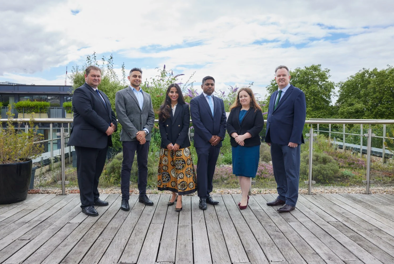 A group of business professionals stand together on an outdoor wooden deck on a cloudy day.