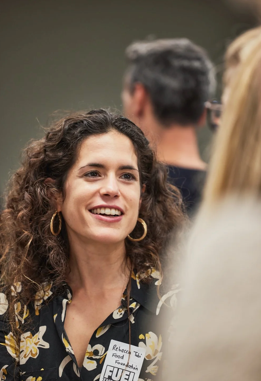 A person with curly dark hair and gold hoop earrings smiles warmly while engaged in conversation.