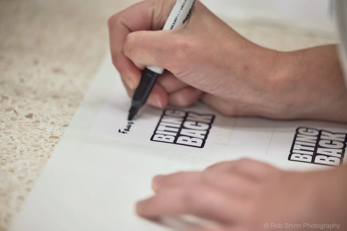 Close-up view of hands writing or drawing on paper with a black pen.