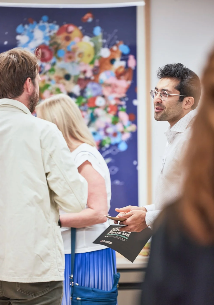 Two people in white and blue attire engaged in conversation at a professional event with colorful artwork in background.