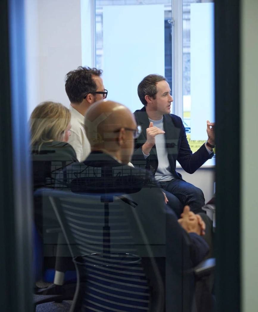 Business professionals seated at tables in a modern office space during a meeting or conference.