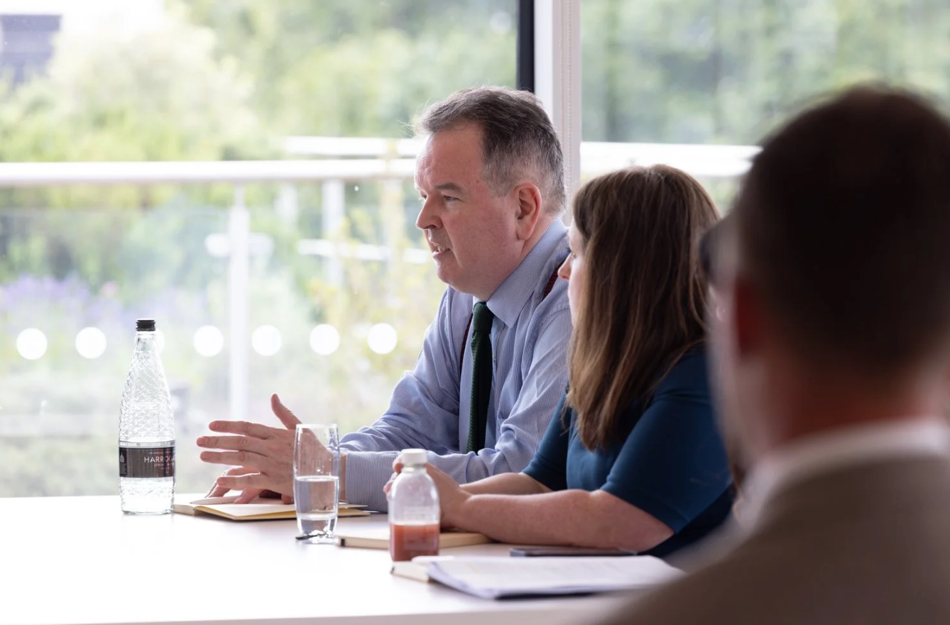 Business professionals sit at a conference table during a meeting in a bright modern office space.