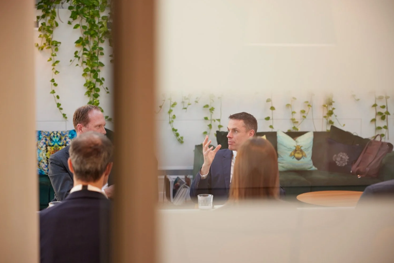 Two people having a conversation in an office setting with green plants and vines decorating the walls.