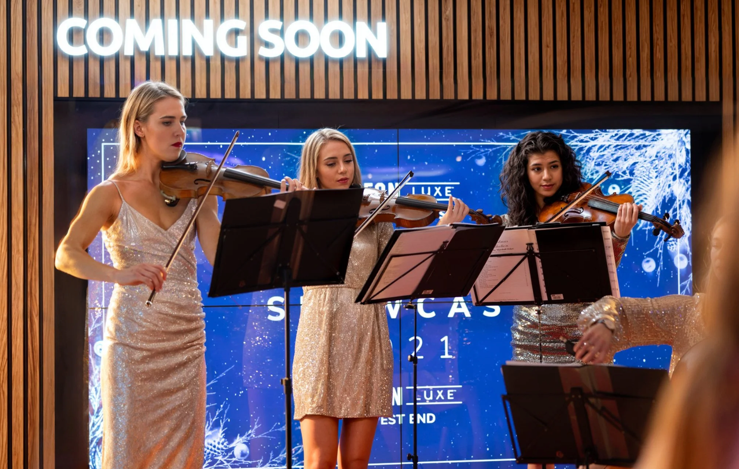 Musicians perform on stage with sheet music stands and blue lighting in the background.