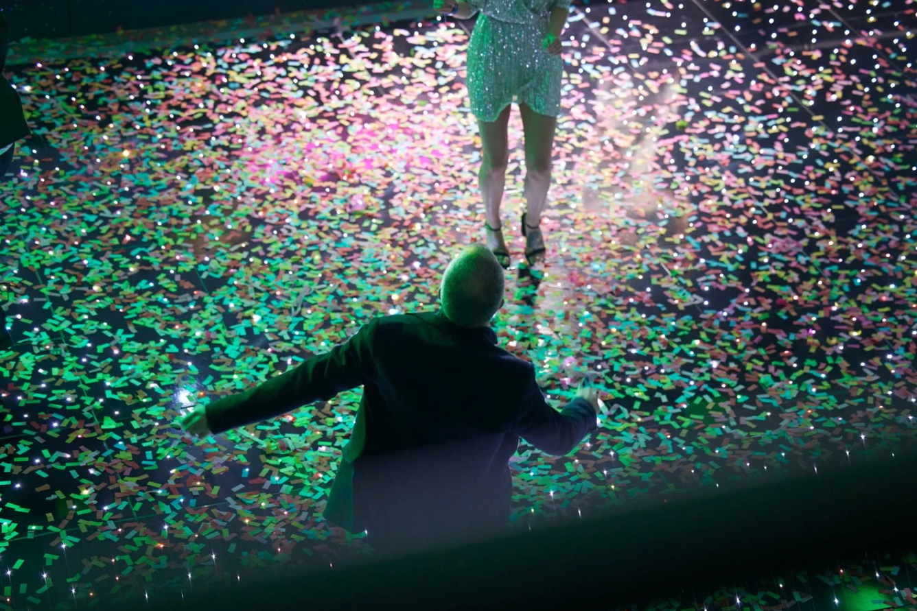 Colorful confetti rains down during a celebration event with teal and pink lighting effects in the background.