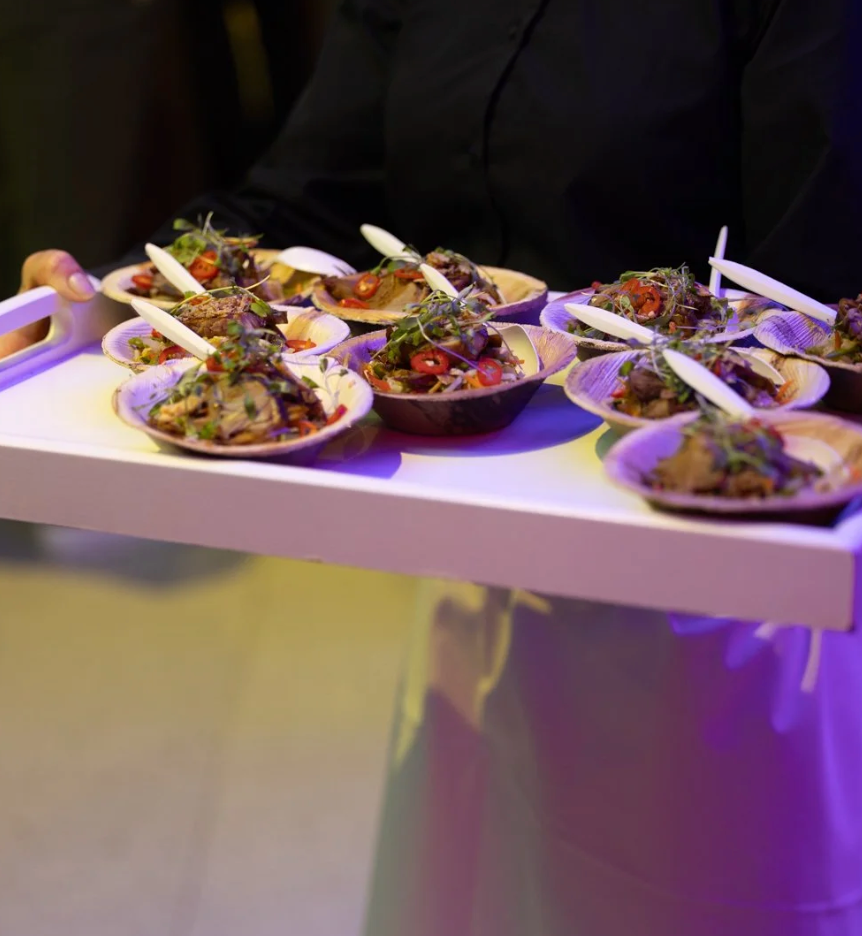Elegant appetizer plates arranged on a white surface with purple ambient lighting showcasing gourmet small bites.