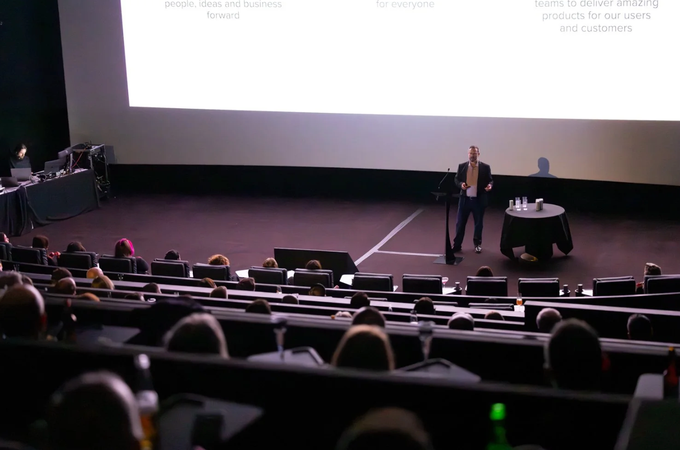 A dark movie theater with rows of empty seats and a large projection screen showing a presentation.