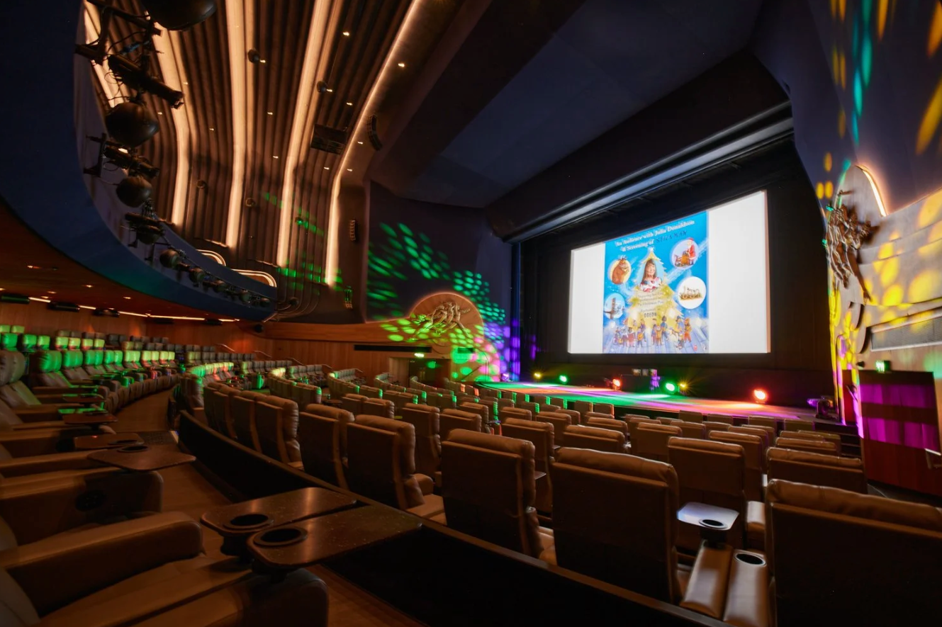 Modern movie theater auditorium with colorful LED lighting and stadium seating showing an animated film on the screen.