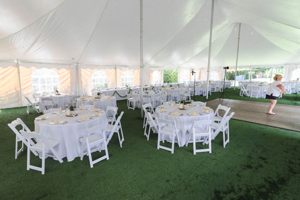 Interior view of an elegant white wedding tent with round tables and chairs arranged for a reception.