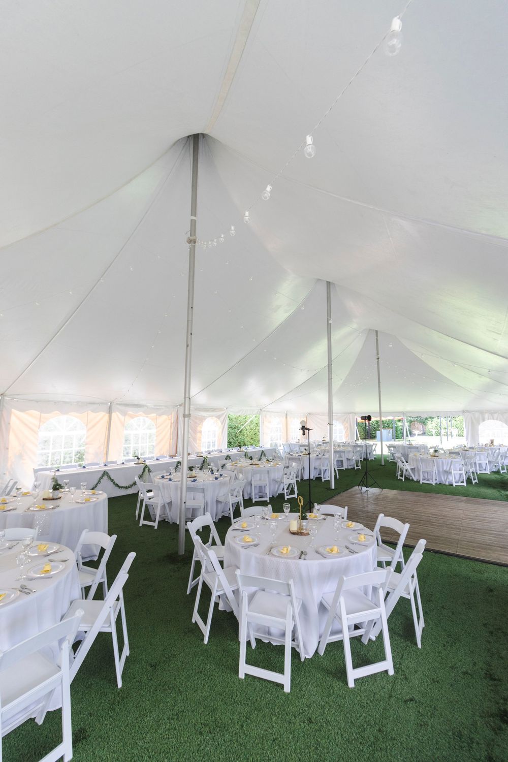 White wedding tent interior set up with round tables and chairs on artificial grass for an elegant outdoor reception.