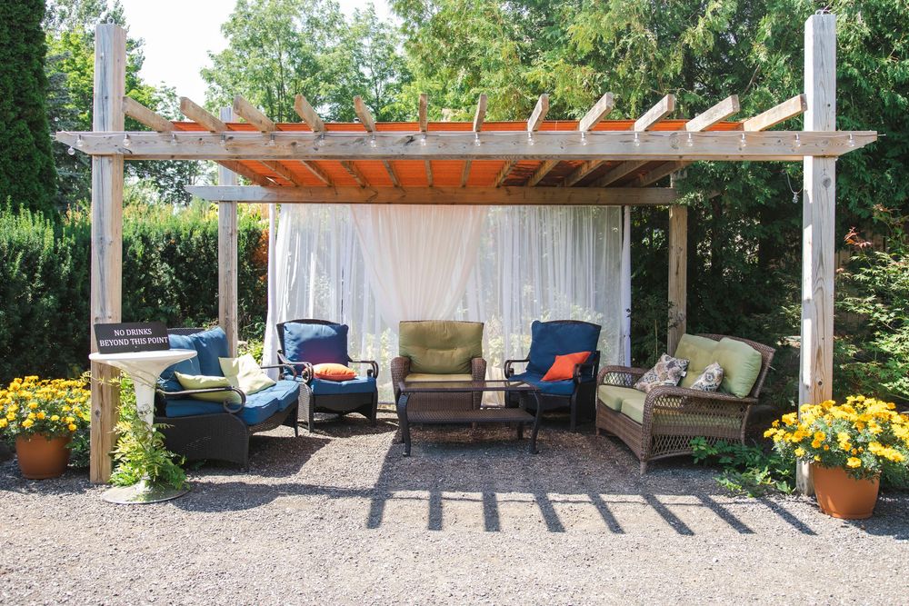 Outdoor patio pergola with white curtains, comfortable seating, and yellow potted flowers creating a cozy backyard retreat.