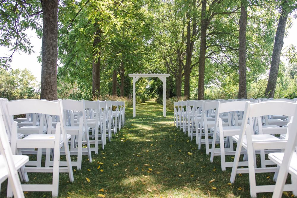 Panoramic view of white folding chairs set up in neat rows for an outdoor wedding in a shaded forest grove.