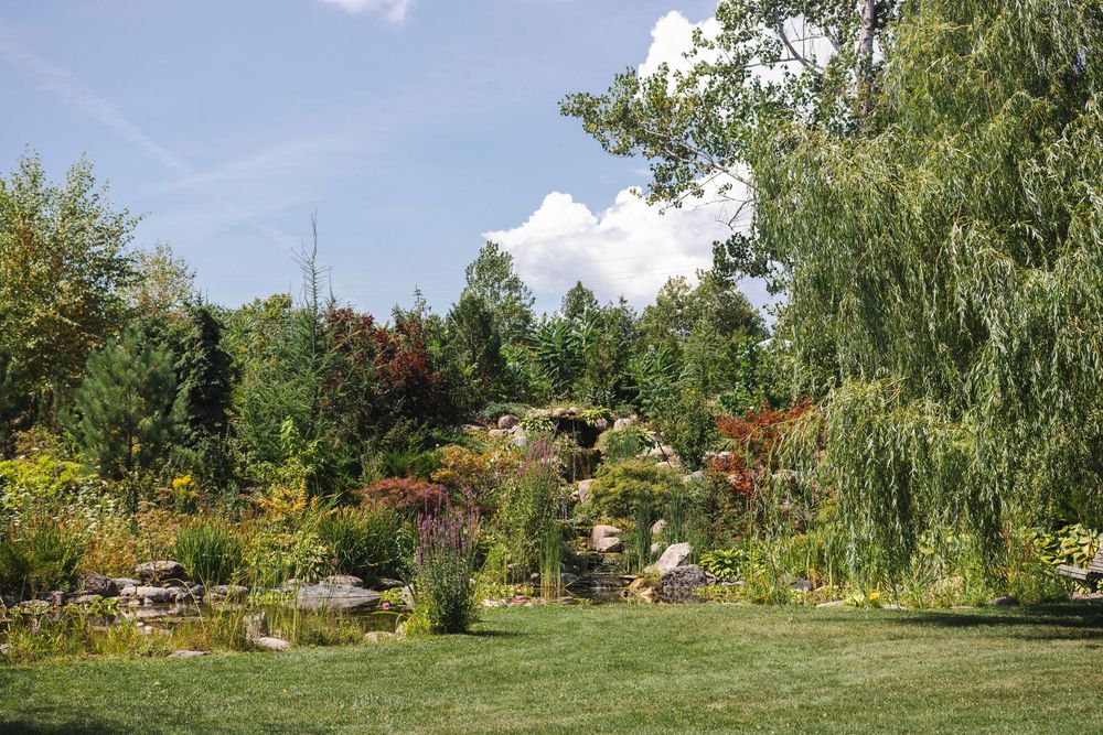 Panoramic view of a lush garden landscape with blooming flowers, trees, and winding paths under a blue summer sky.