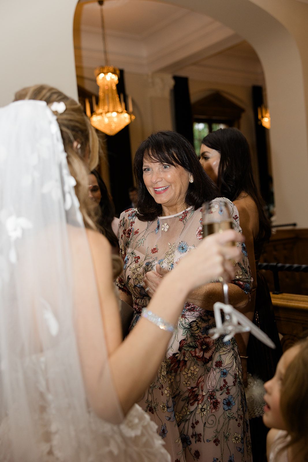 A wedding celebration scene with guests mingling under elegant chandeliers in an ornate indoor venue.