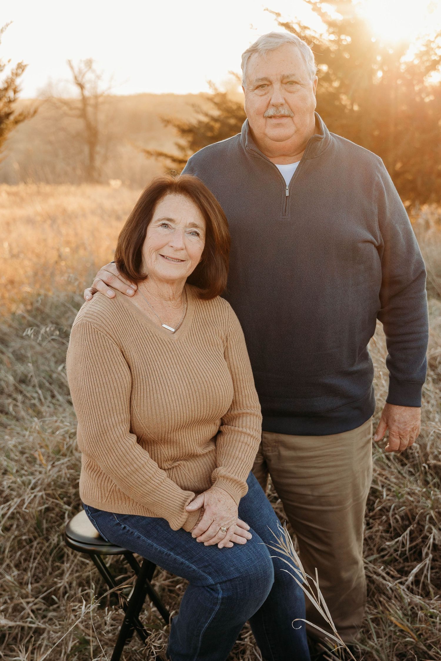 A couple sits together outdoors during golden hour in casual autumn attire.