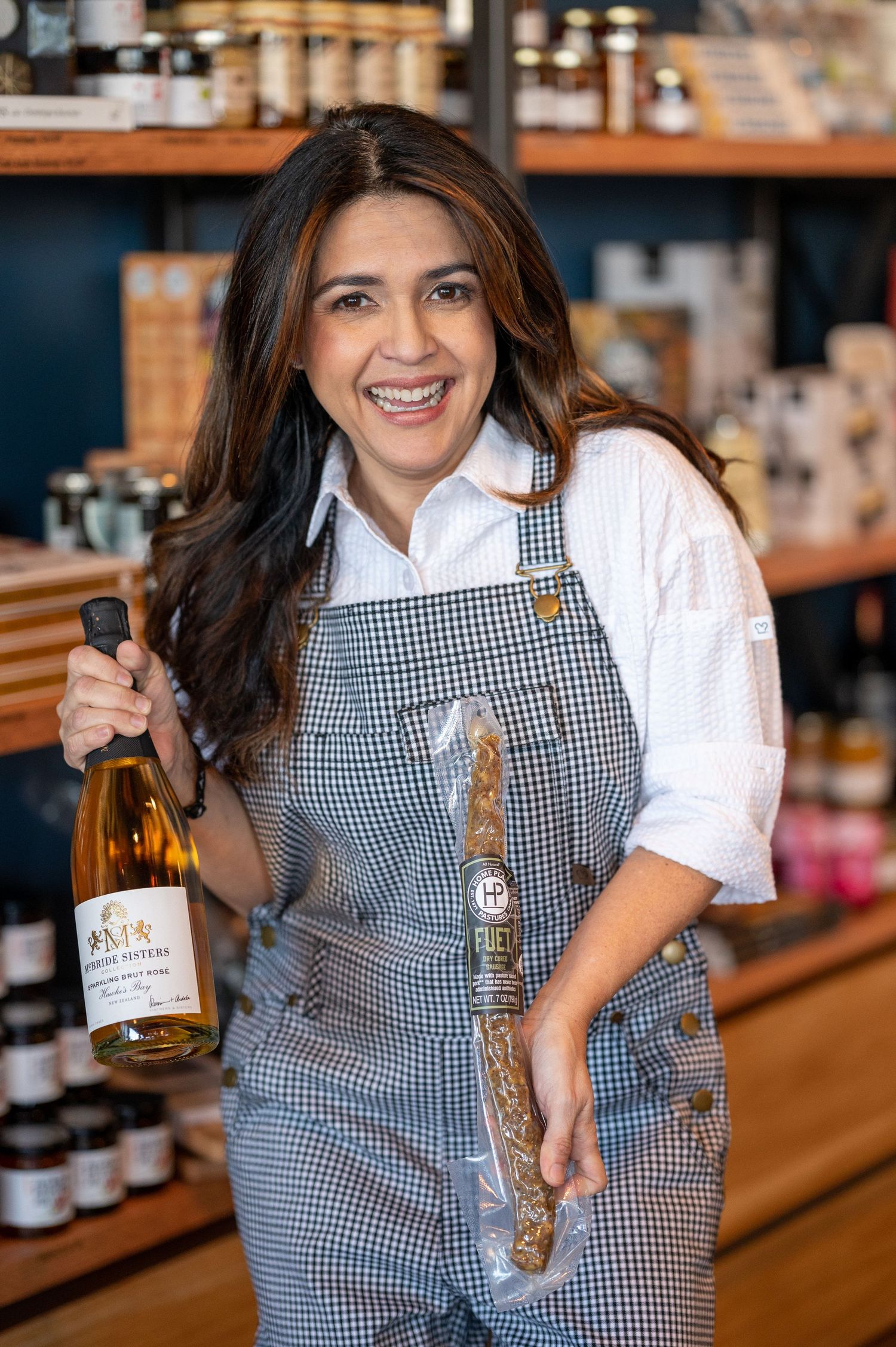 Server in checkered apron showcases bottles of spirits at a bar counter.