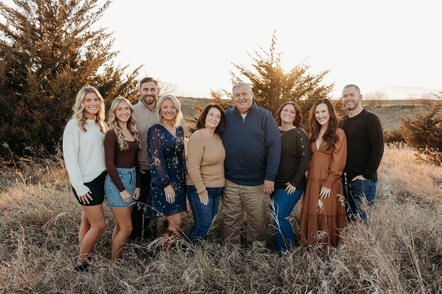 A group of people gathered outdoors at sunset in casual attire for a family photo session.