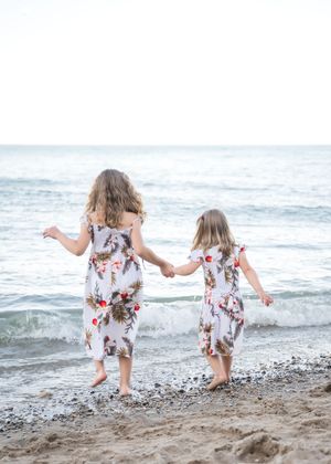 Two children in matching floral dresses play together at the beach near the ocean waves.