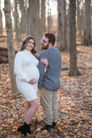 A couple dances playfully among fallen autumn leaves in a forest setting during a romantic photoshoot.