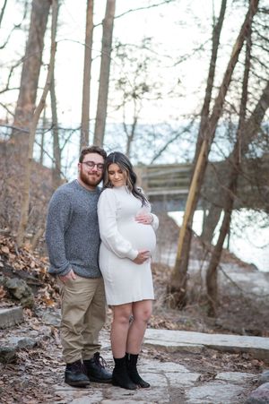 A couple embraces while standing in a wooded area near a lake during an outdoor photo session.