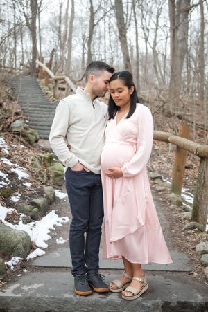 A romantic couple shares tender moments on stone steps in a snowy winter forest setting wearing pink and white outfits.
