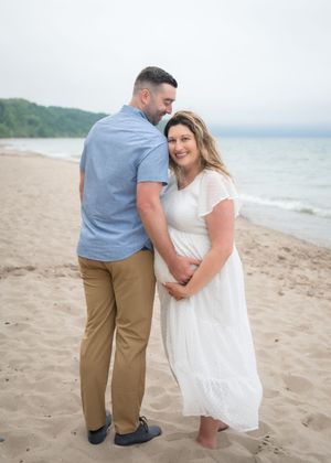 A couple shares an intimate moment together on a peaceful beach with water and hills in the background.