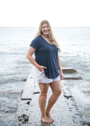 Person in casual attire walking along a rocky beach shoreline with waves crashing in the background.