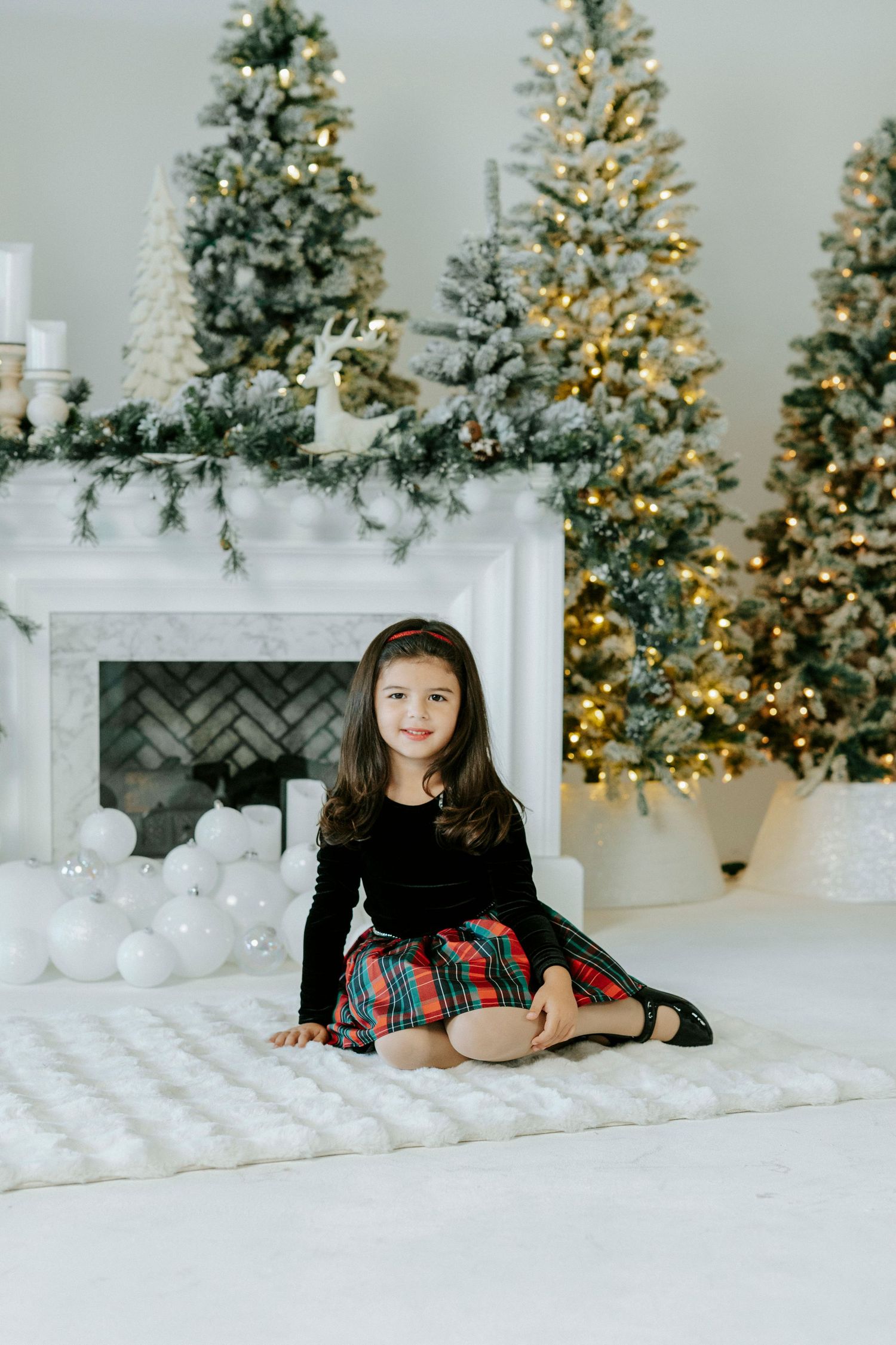 Holiday photo session setup with decorated Christmas trees and white decor in a bright studio setting.