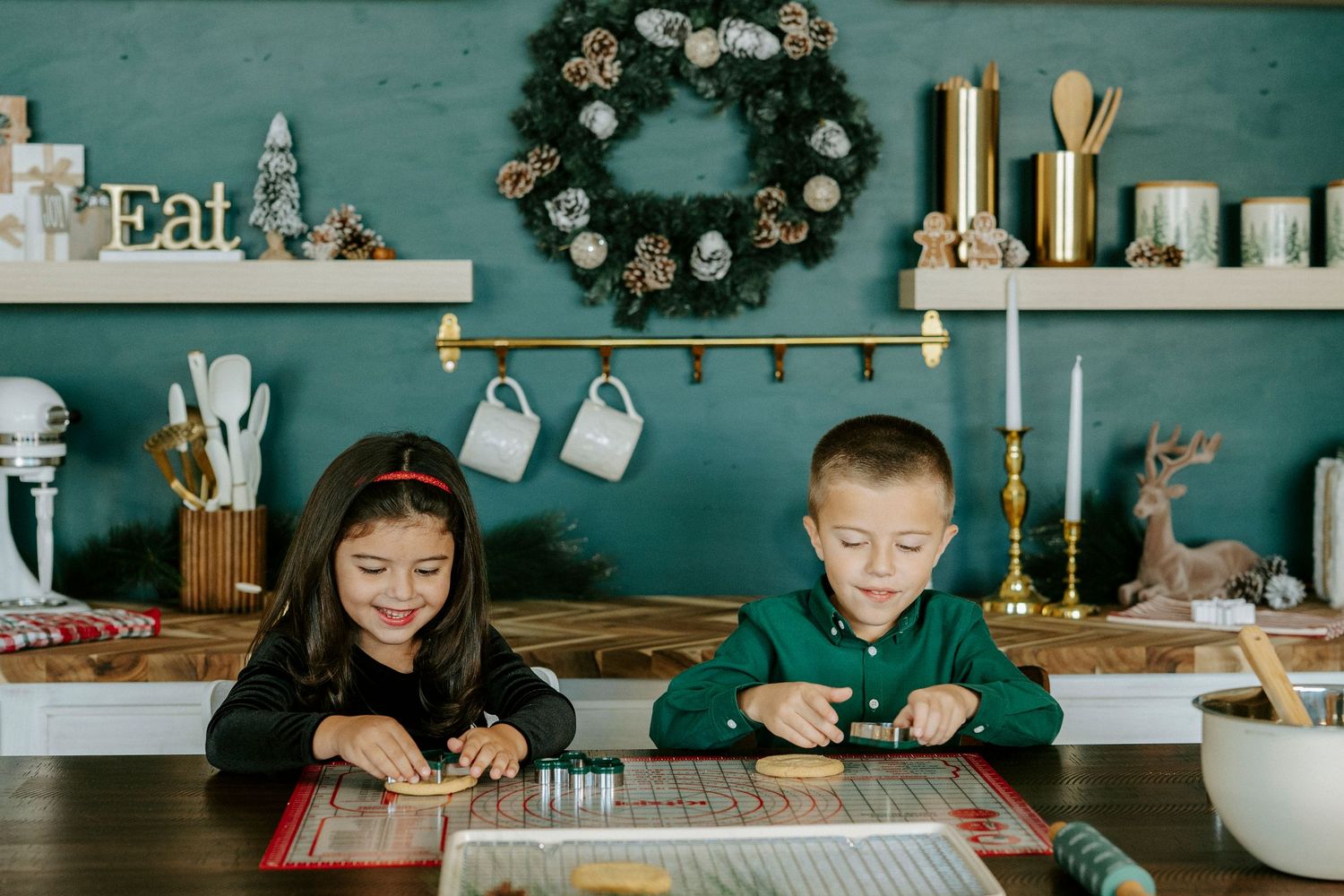 Two people sit at a rustic farmhouse table with teal walls and holiday decor in a cozy kitchen setting.