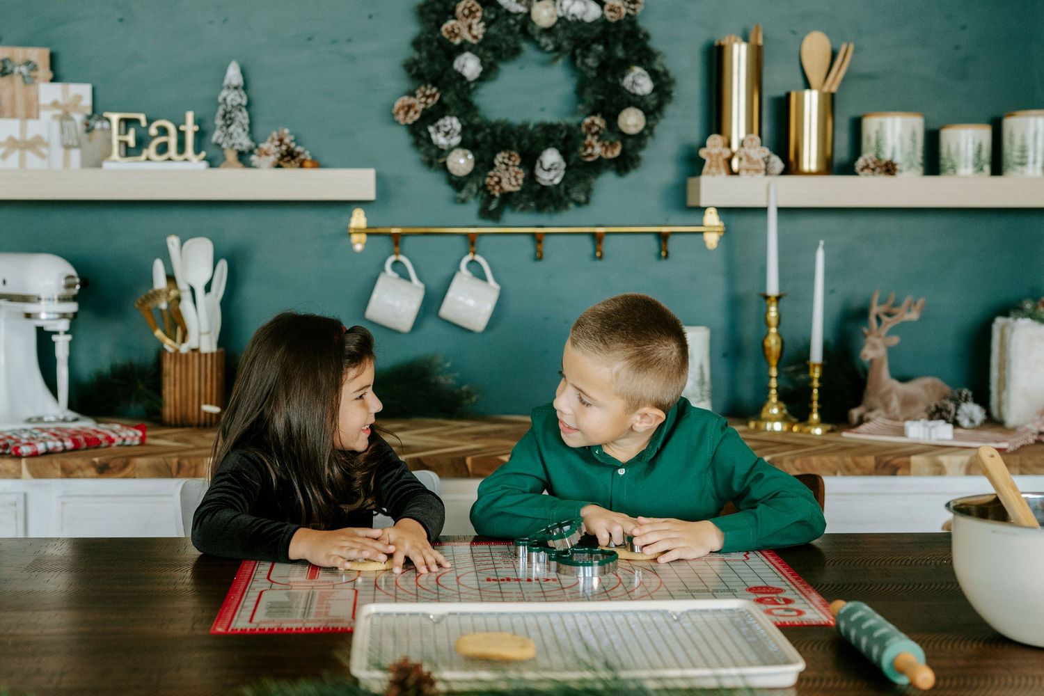 Two people share a moment at a farmhouse table with teal walls and holiday decorations in the background.