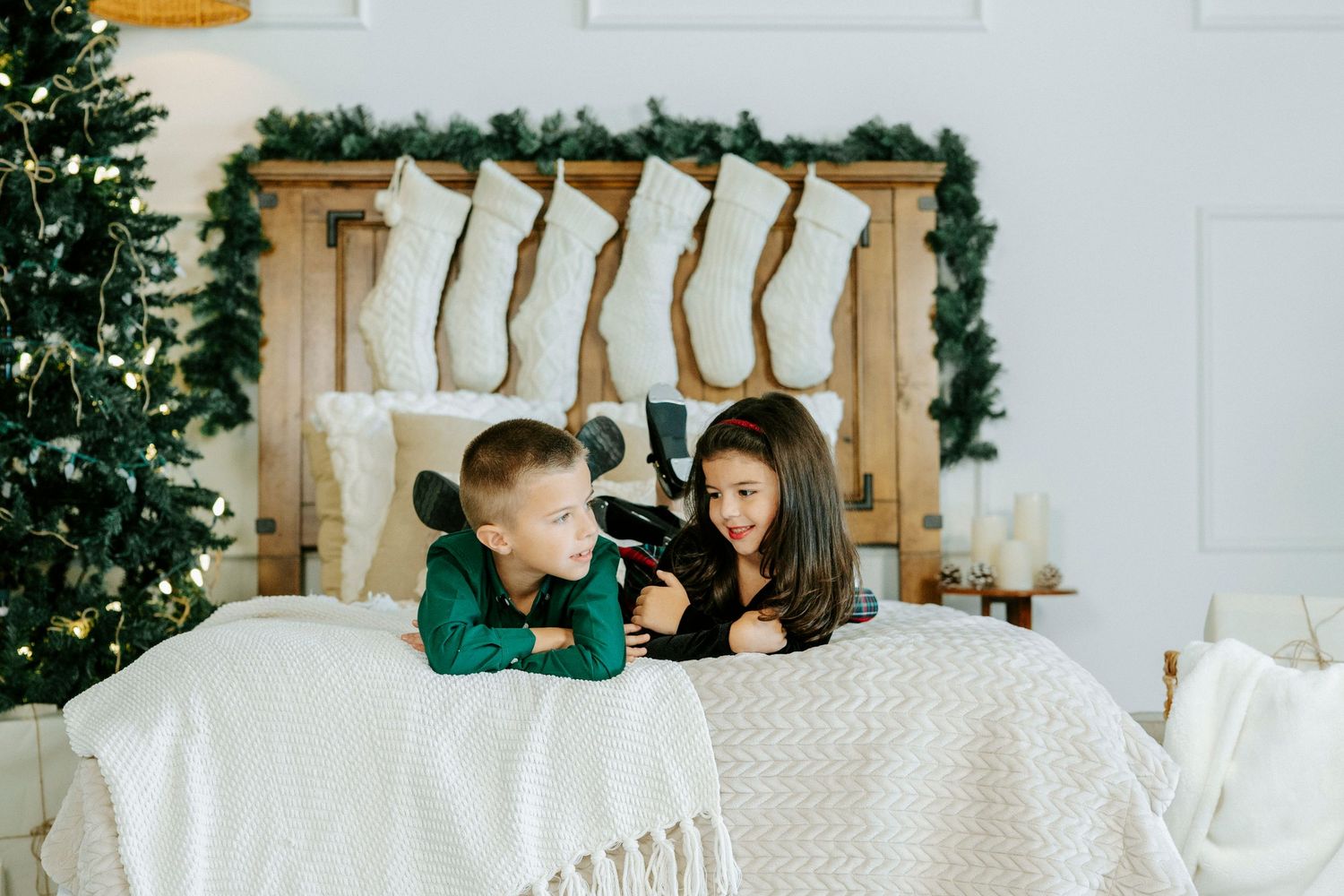 A cozy winter bedroom decorated with white bedding, greenery, and rustic wooden accents for the holidays.