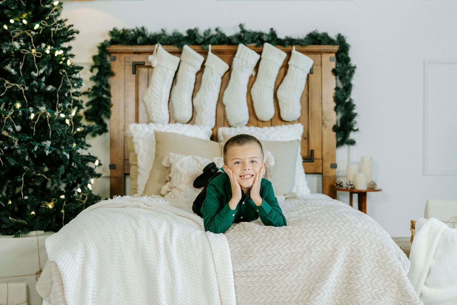 White duvet covers and pillows arranged on a bed with green accents and a Christmas tree in the background.