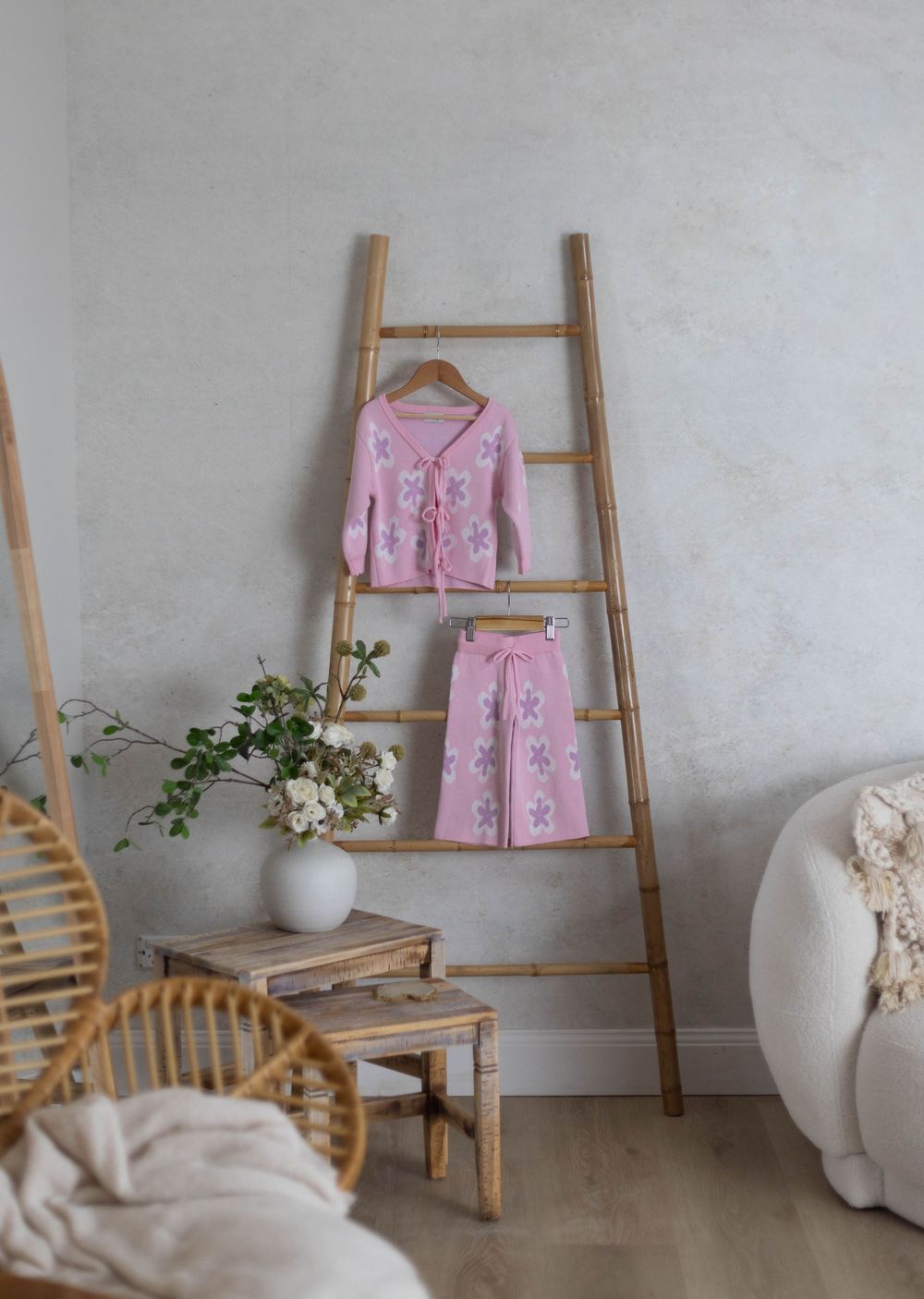 Pink floral knit children's pajama set displayed on a bamboo ladder in a cozy, neutral-toned room.