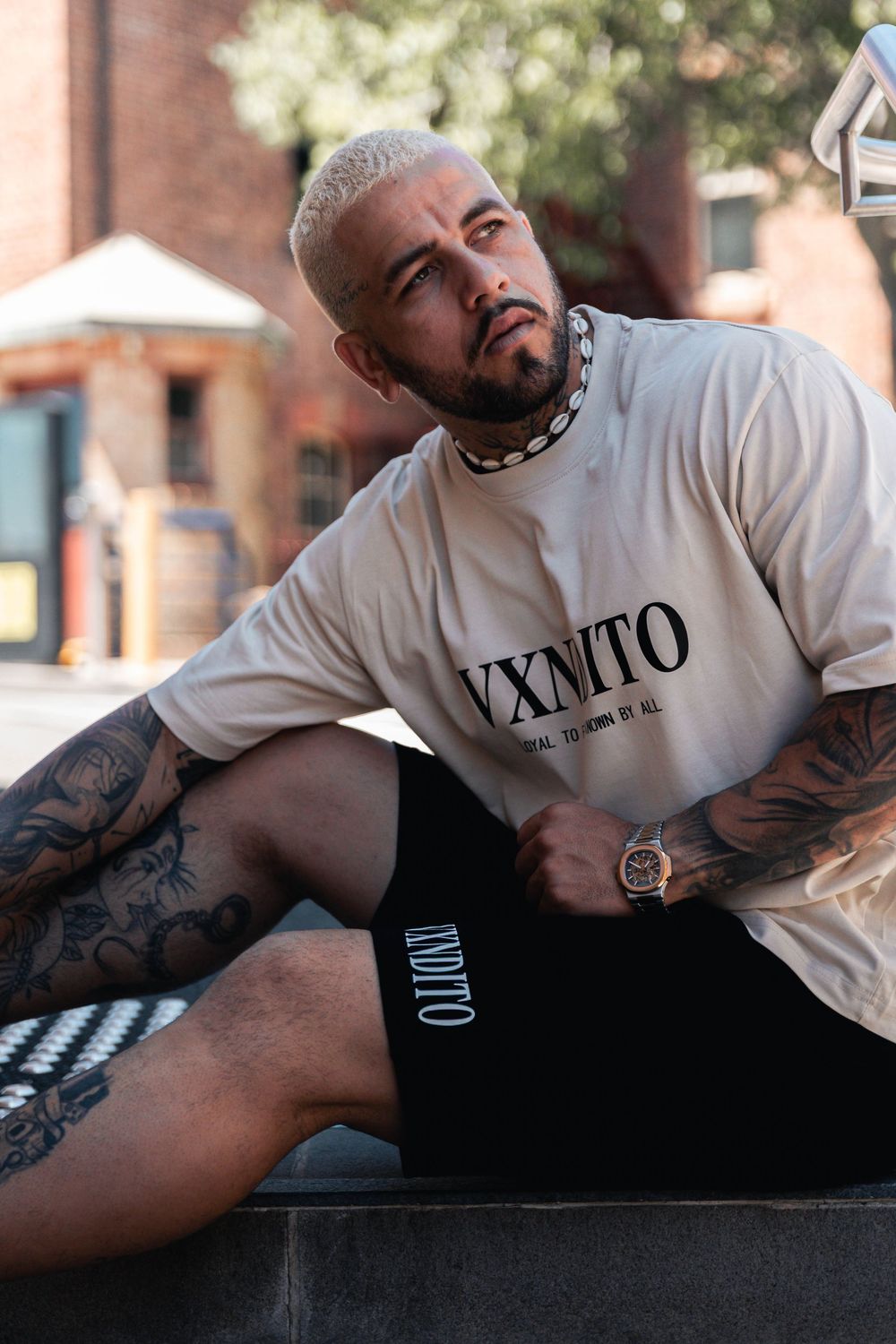 Person in white t-shirt with tattoos lounging on dark surface in artistic photo series.