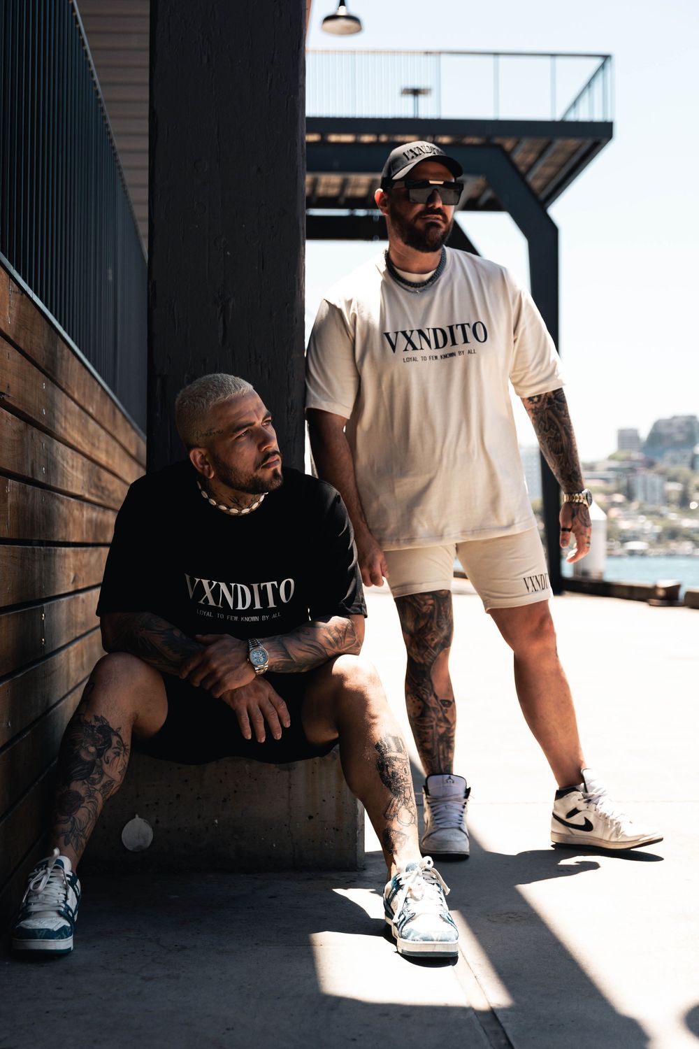 Dramatic lighting highlights streetwear fashion against dark architectural background.
