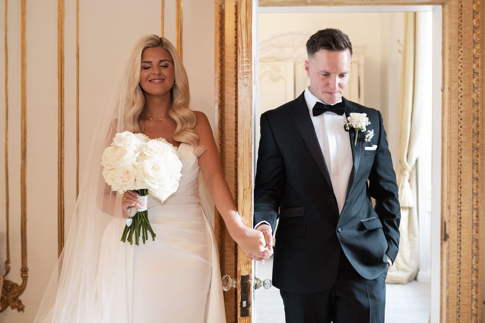 A wedding couple walks through an elegant hallway with ornate gold trim and mirrors creating a romantic atmosphere.