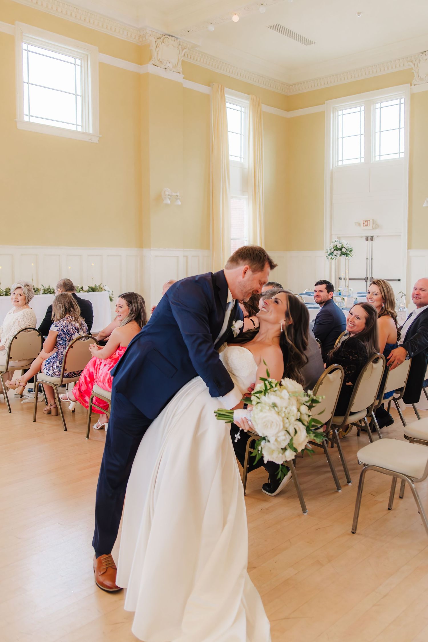 A sequence of wedding photos showing a couple dipping and kissing in a bright, elegant room with guests seated in chairs.